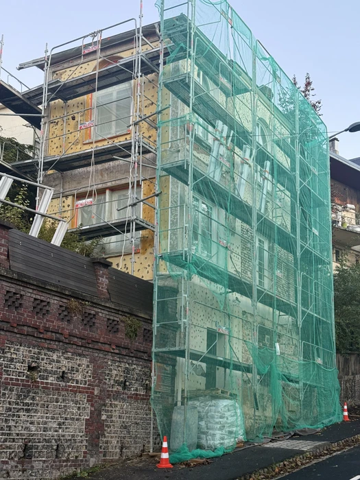 Chantier de rénovation de façade en extérieur avec échafaudages métalliques tubulaires et bâches de protection vertes couvrant un bâtiment en pierre